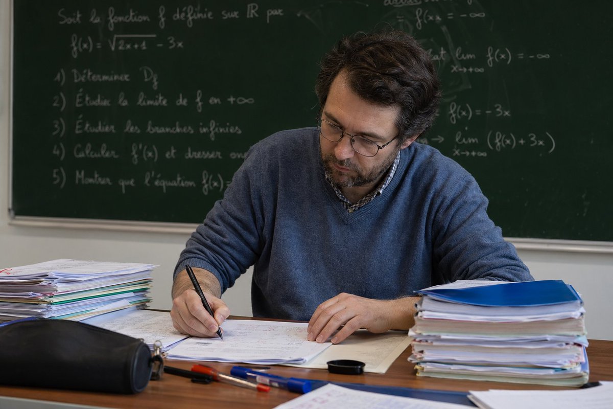 Professeur de mathématiques corrigeant des copies en classe